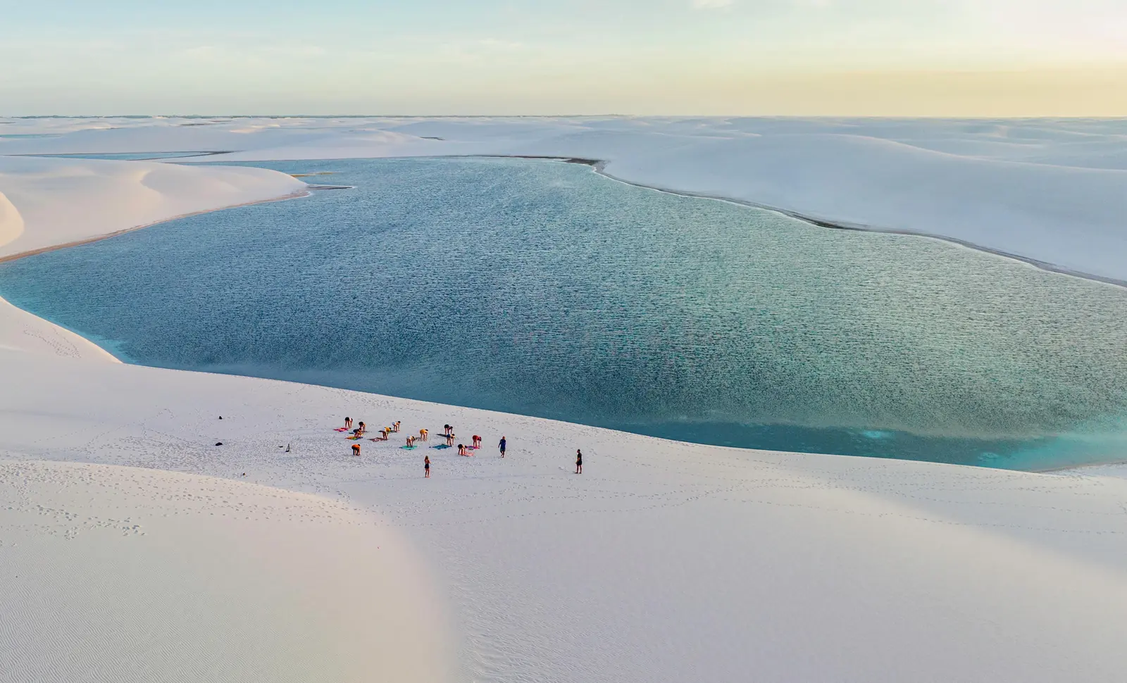 Caminhantes cruzando lagoas de água clara nos Lençóis Maranhenses